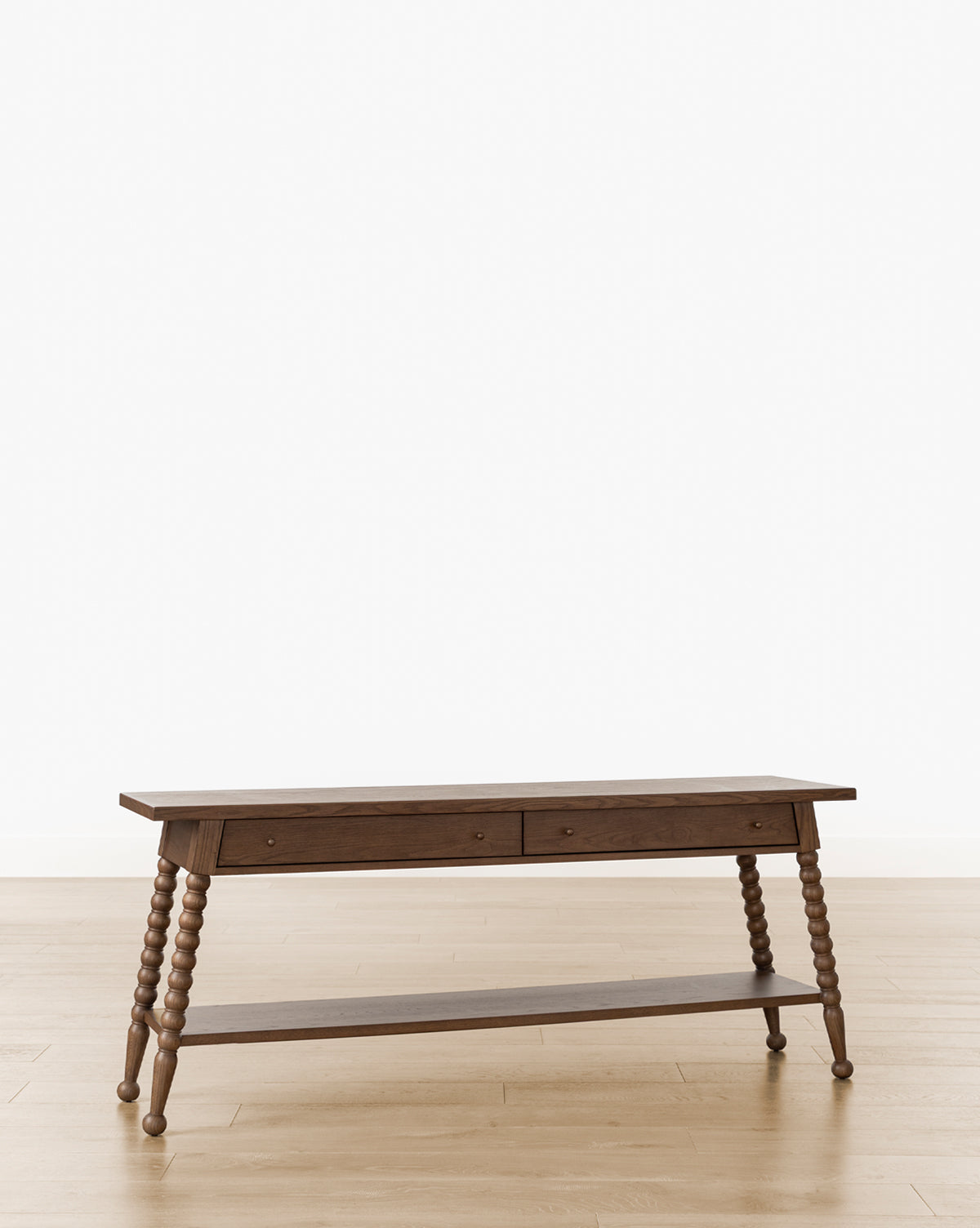 The Heathcliff Console, finished in walnut oak with two drawers, intricately turned bobbin-style legs, and a lower shelf, stands on a light wooden floor against a plain white background by McGee & Co.