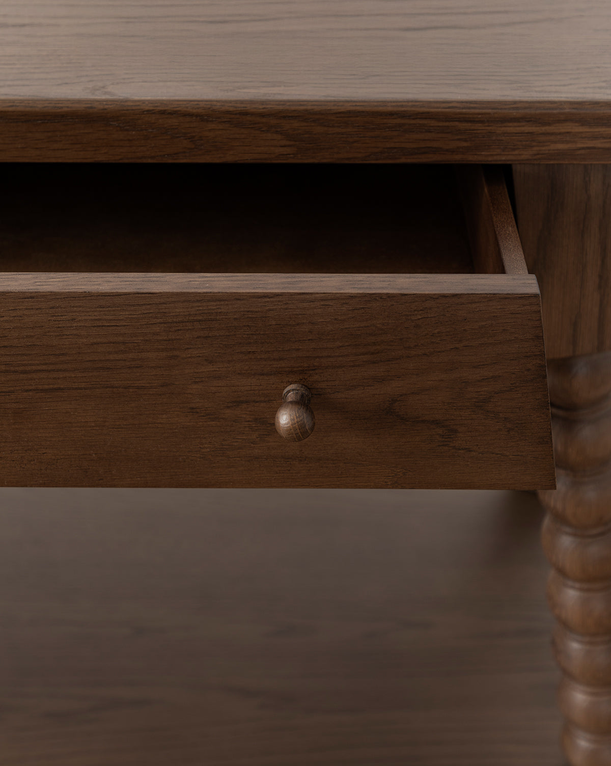 A close-up of the Heathcliff Console shows a partially open drawer with a round wooden knob and carved bobbin-style legs, all in a rich walnut oak finish, by McGee & Co.