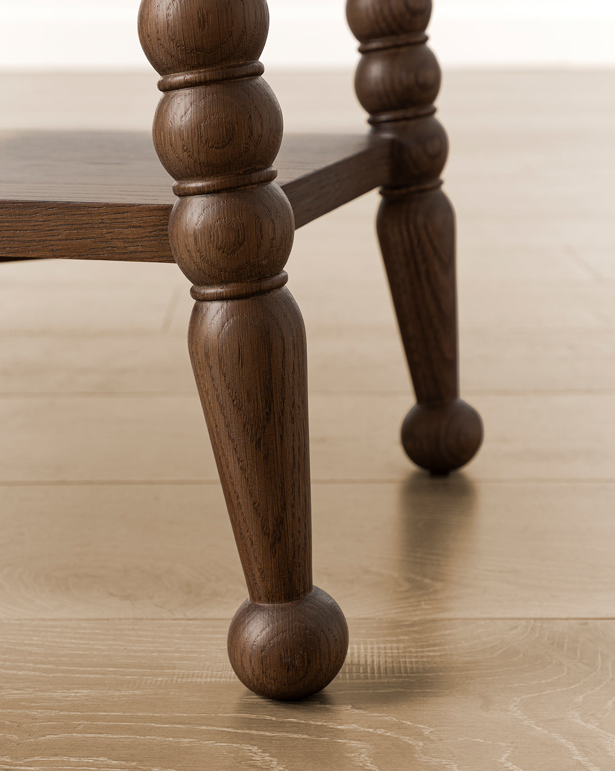 Close-up of two Heathcliff Console bobbin-style legs with a rounded, carved design, standing on a light wood floor. A lower wooden shelf is partially visible between the legs, by McGee & Co.