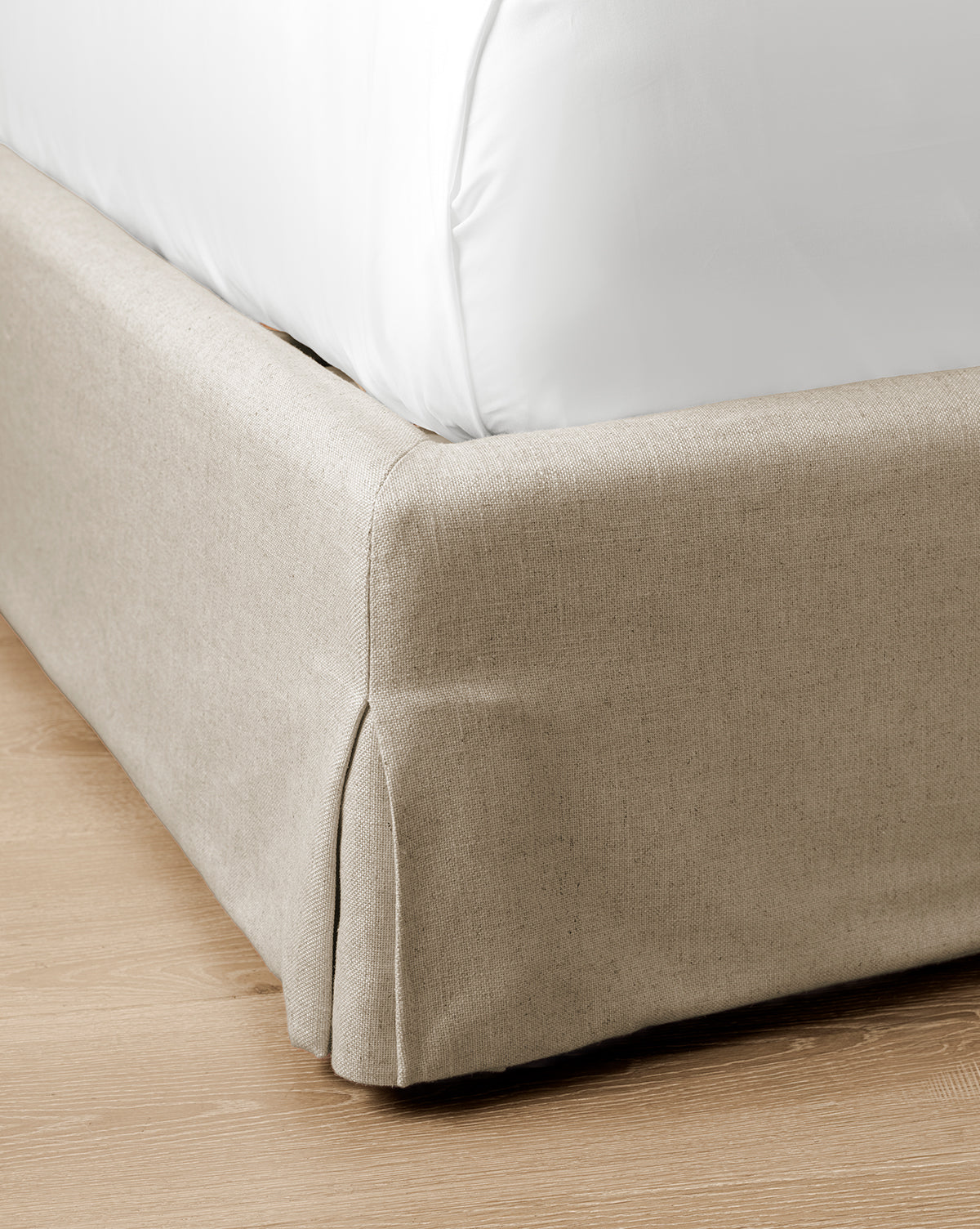 Close-up of the corner of the Henrietta Bed (Ready to Ship) in beige upholstery with a white bedsheet, set on a light wooden floor—a stylish detail for effortless bedroom decor, by McGee & Co.