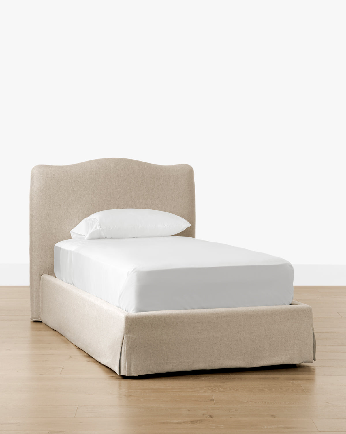 The Henrietta Bed (Ready to Ship), featuring beige upholstery and a curved headboard, is shown with white bedding on a light wood floor—an elegant choice for bedroom styling against a plain white background, by McGee & Co.