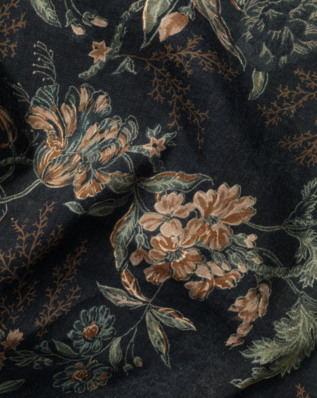 A close-up of the Hestercombe Tablecloth shows its dark fabric with a detailed vintage floral pattern in peach, green, and beige. The slightly wrinkled texture adds depth to the botanical design, by McGee & Co.