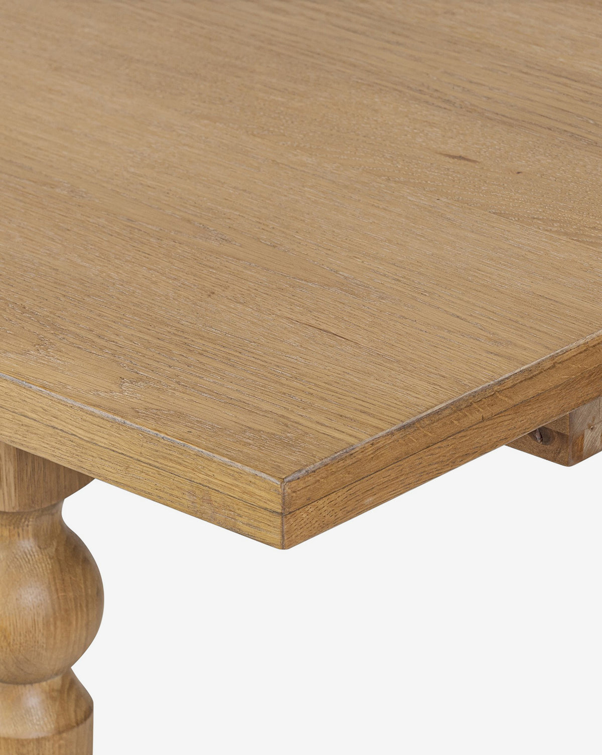 Close-up of the Kyler Oak Extension Dining Table corner, featuring a smooth, light brown surface and a turned leg against a plain white background, by McGee & Co.