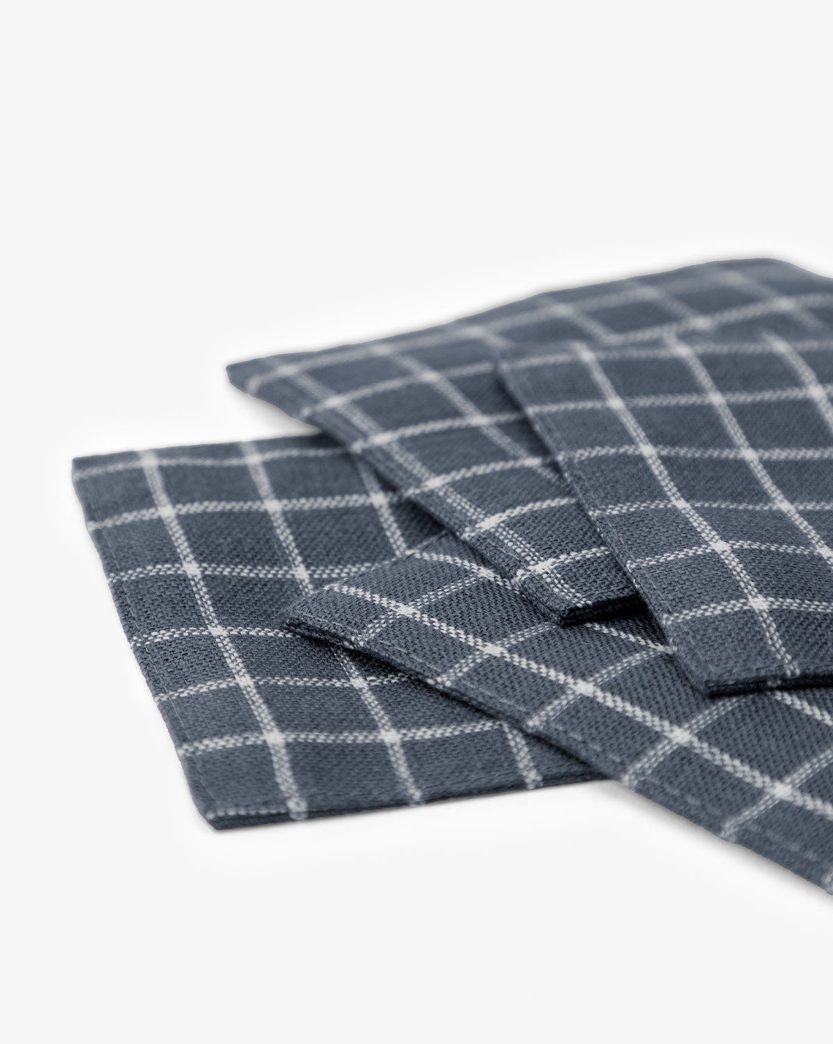 A close-up of Lancaster Linen Coasters (Set of 4) in dark gray with a white checkered pattern, neatly stacked on a white surface—perfect absorbent coasters for stylish table settings, by McGee & Co.