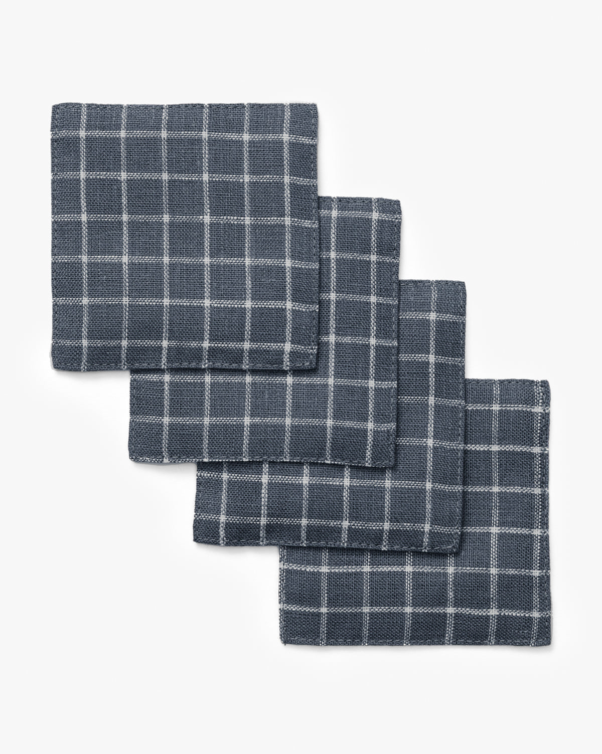 A set of four Lancaster Linen Coasters with a navy blue and white checkered pattern is displayed in a slightly overlapping, diagonal stack on a white background, by McGee & Co.