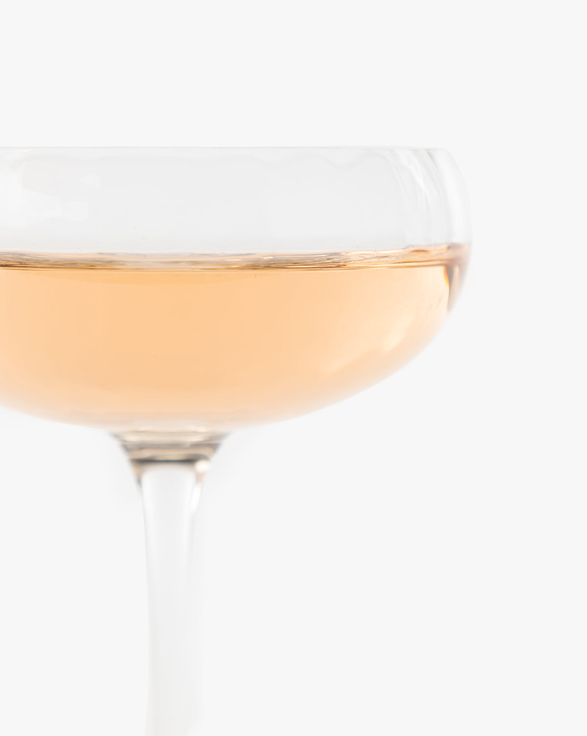 A close-up of the Langford Coupe (Set of 4) filled with pale pink sparkling wine, showing only the upper half of this elegant glassware against a plain white background, by McGee & Co.