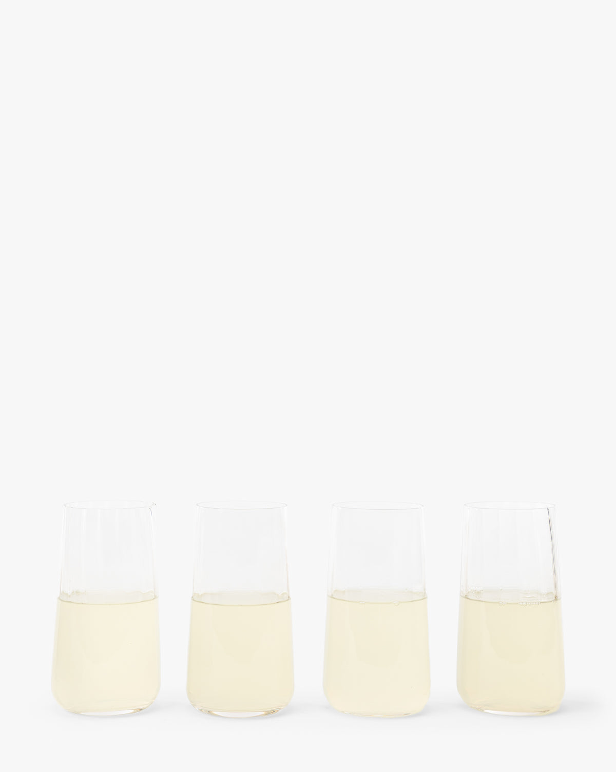 A set of four Langford Highball Glasses, each filled with a light yellow liquid, arranged in a row on a plain white background by McGee & Co.