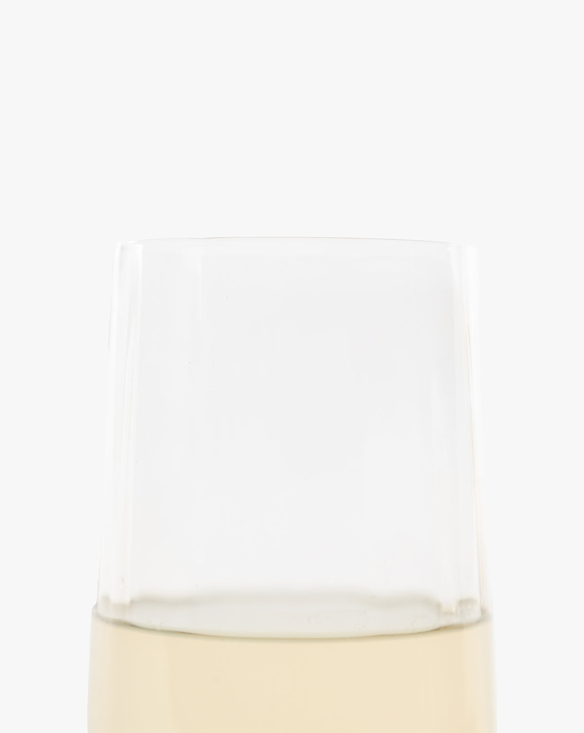 A close-up of the top half of a Langford Highball Glass, filled with pale yellow liquid, set against a plain white background. Only the upper portion of the clear glass is visible by McGee & Co.