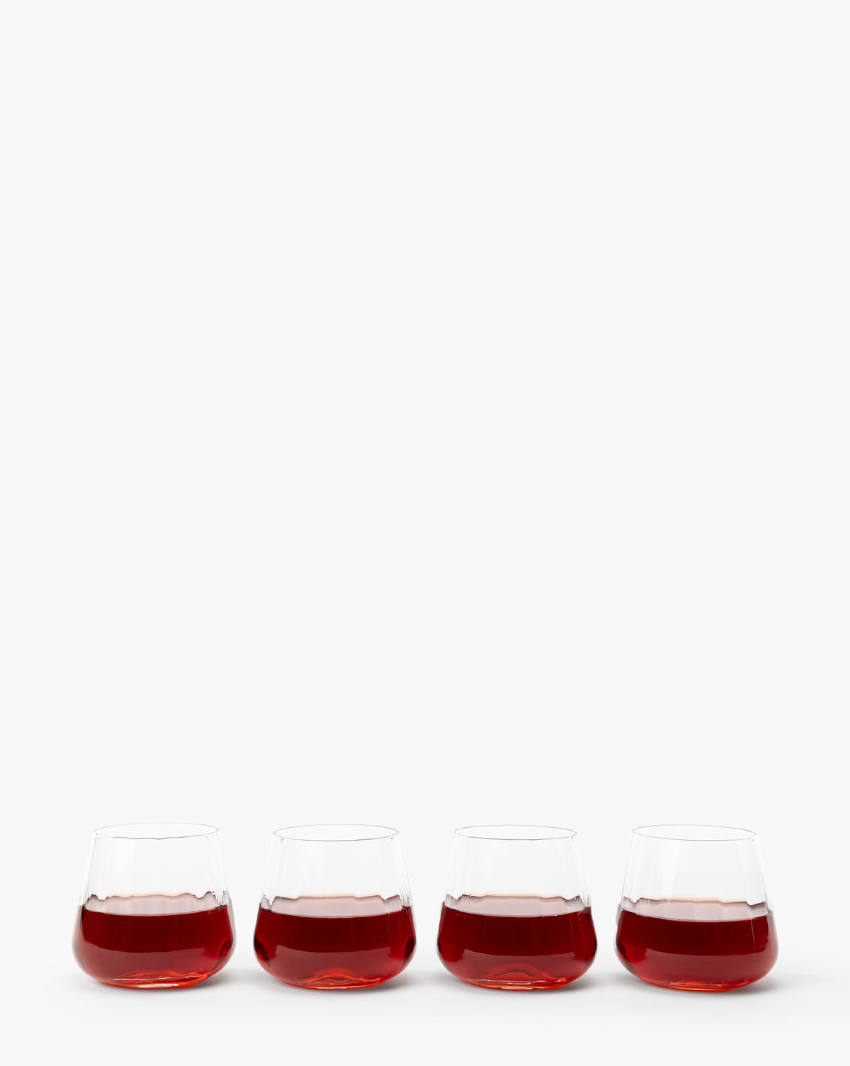 A set of four Langford Tumblers, each filled with red wine, are arranged in a row against a plain white background—an elegant addition to any table setting, by McGee & Co.