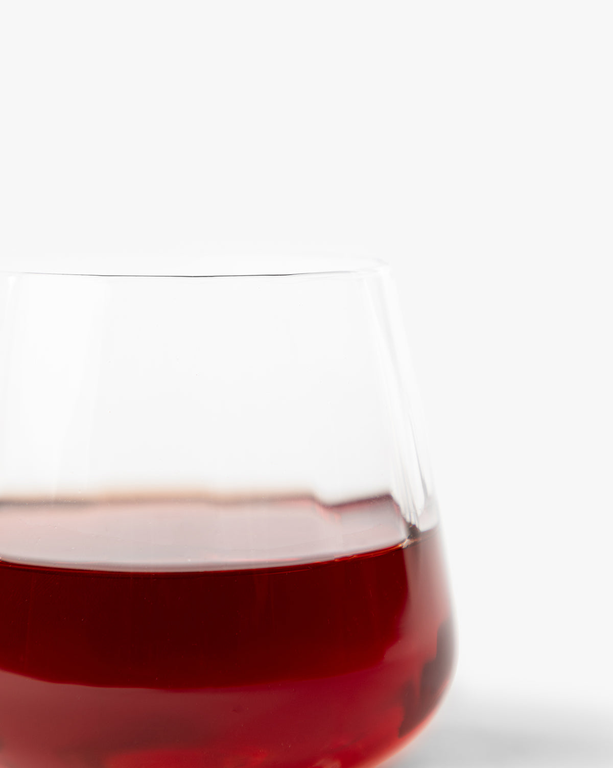 A close-up of a partially filled Langford Tumbler from the Langford Tumblers (Set of 4) highlights the rich red wine color and elegant design against a plain white background, emphasizing refined taste and stylish glassware by McGee & Co.