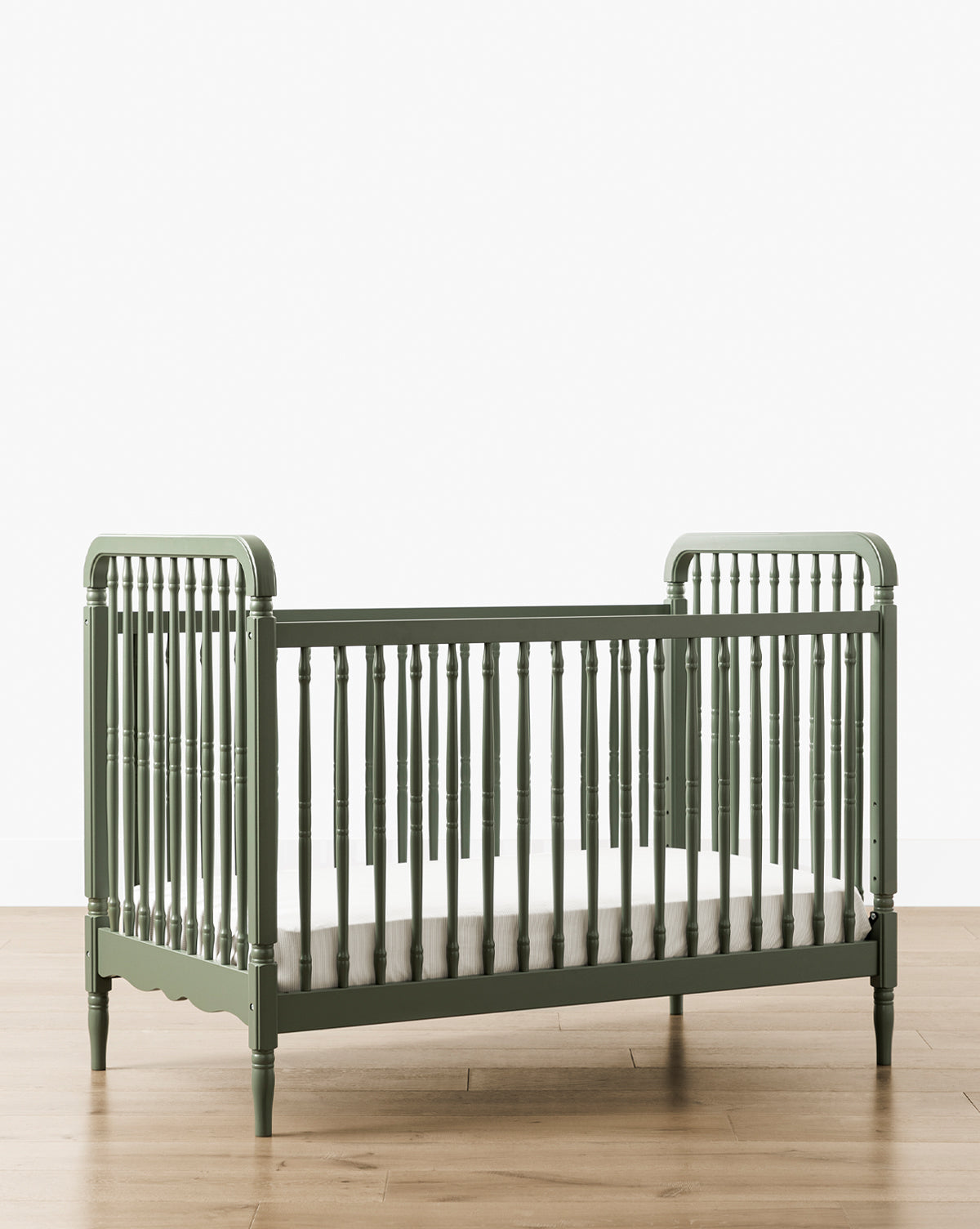 The Liberty 3-in-1 Convertible Spindle Crib w/Toddler Bed Conversion Kit, in green solid pine, with spindled sides and ends, is displayed on a light wood floor against a plain white background by McGee & Co.