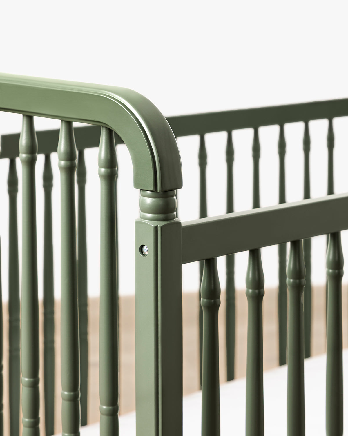 Close-up of the Liberty 3-in-1 Convertible Spindle Crib w/Toddler Bed Conversion Kit, shown in green solid pine with vertical slats and rounded edges, set against a plain light background by McGee & Co.