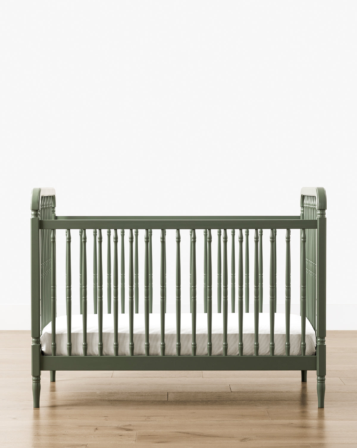 The Liberty 3-in-1 Convertible Spindle Crib w/Toddler Bed Conversion Kit in green solid pine, featuring vertical slats and a white mattress, sits on a light wood floor against a plain white wall, by McGee & Co.