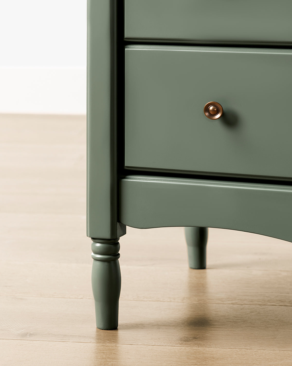 Close-up of the Liberty 6-Drawer Assembled Dresser made from sustainable pine, featuring turned legs, two drawers with round brass knobs, set on a light wood floor against a white wall, by McGee & Co.