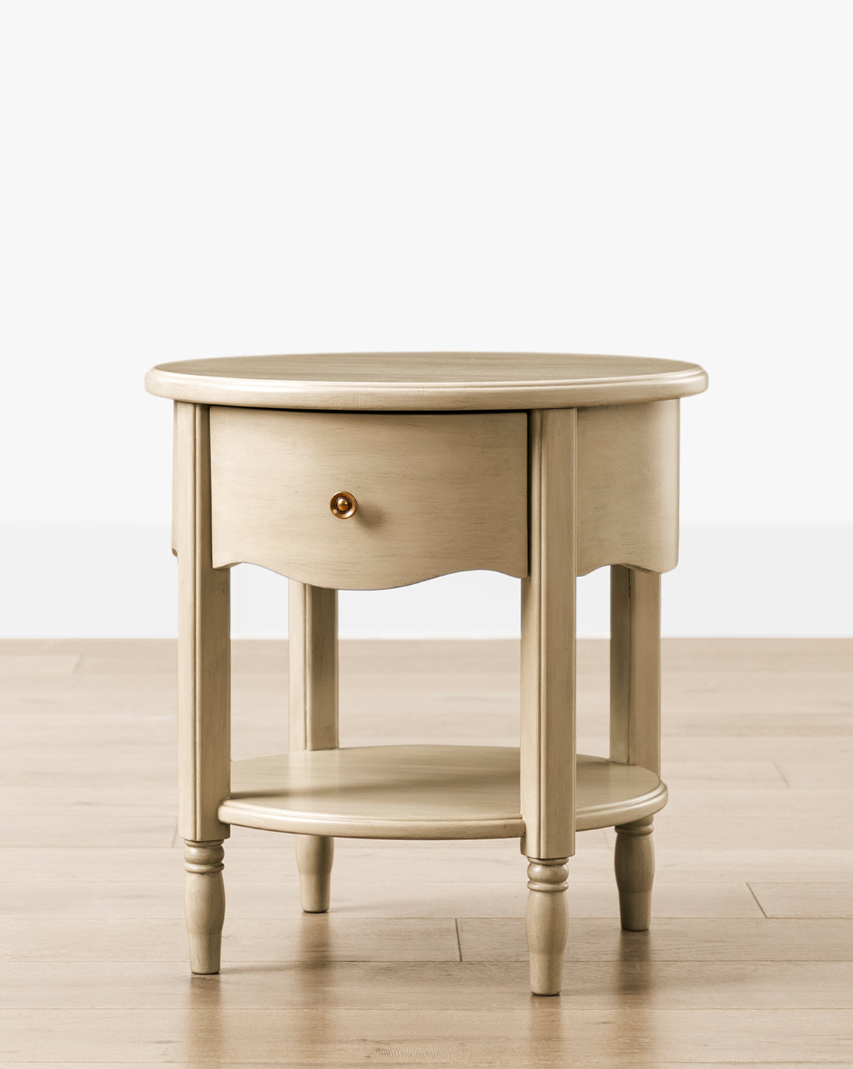 The Liberty Nightstand features a round, light wood design with a single drawer, lower shelf, four turned legs, and a small round knob—perfect for nurseries and GREENGUARD Gold Certified for healthier indoor air, by McGee & Co.