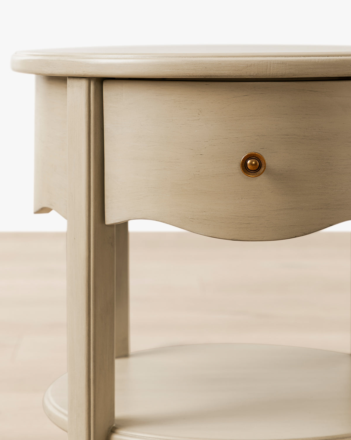 The Liberty Nightstand is a round wooden table with a curved-front drawer and lower shelf in light beige—ideal for nurseries and GREENGUARD Gold Certified for cleaner indoor air, by McGee & Co.
