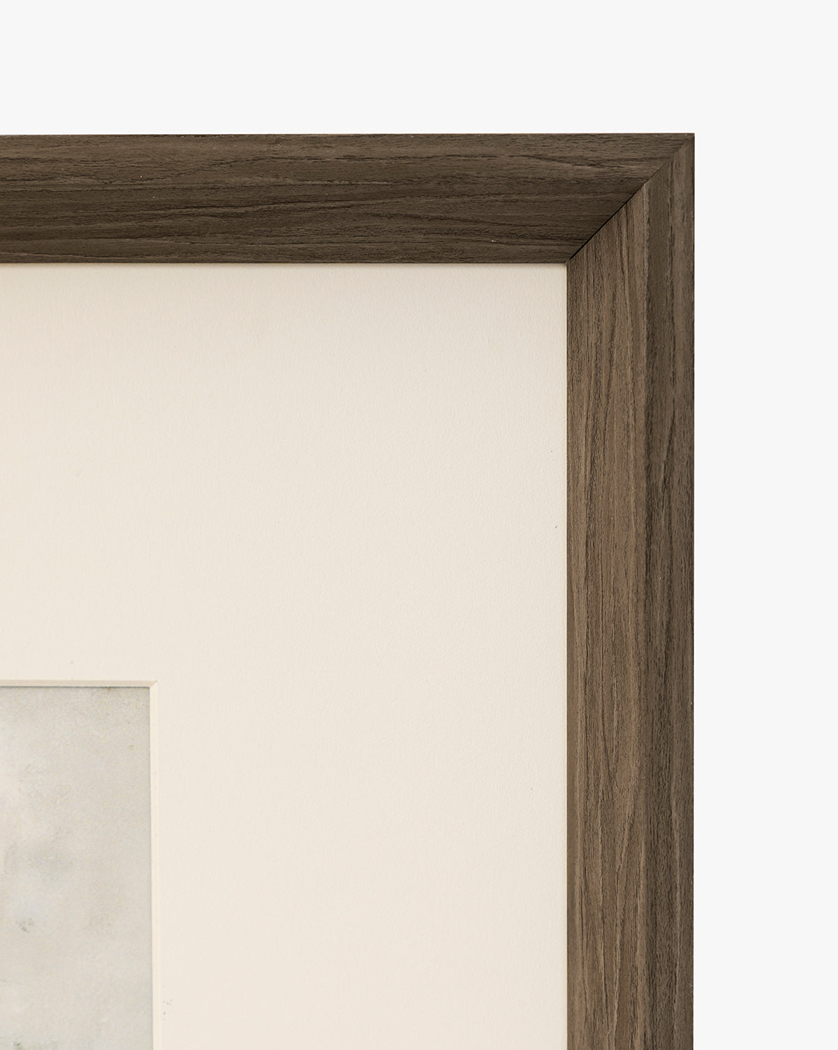 Close-up of the top right corner of a walnut woodgrain frame with a white mat and partially visible Marshland artwork, set against a plain white background, by McGee & Co.