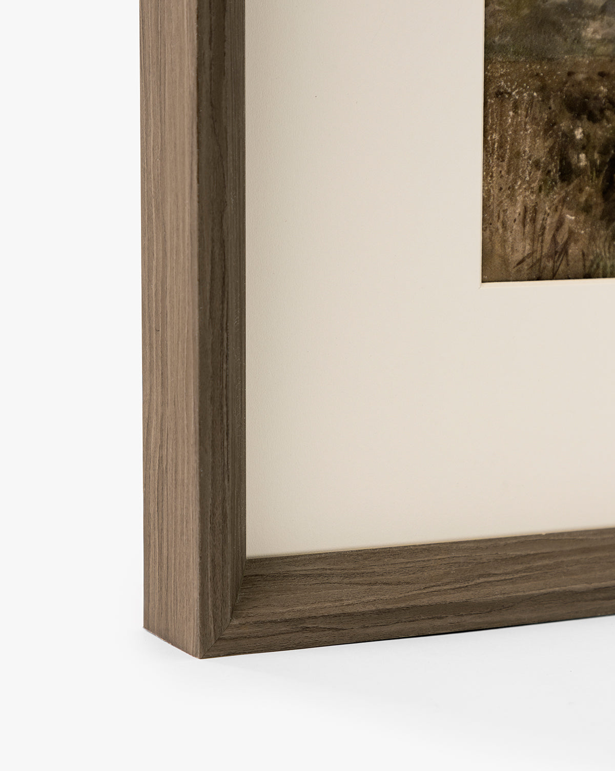 Close-up of the corner of a walnut woodgrain frame with a light brown finish, showcasing part of the Marshland matted giclee on paper against a white background, by McGee & Co.