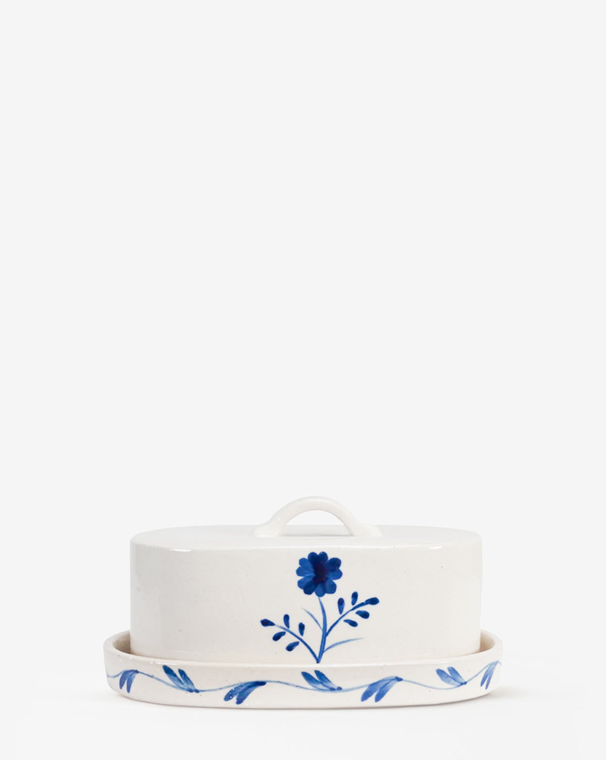 The Mary Hand-Painted Butter Dish is a white stoneware dish with a lid, featuring blue floral designs and a top handle, displayed on a plain white background, by McGee & Co.