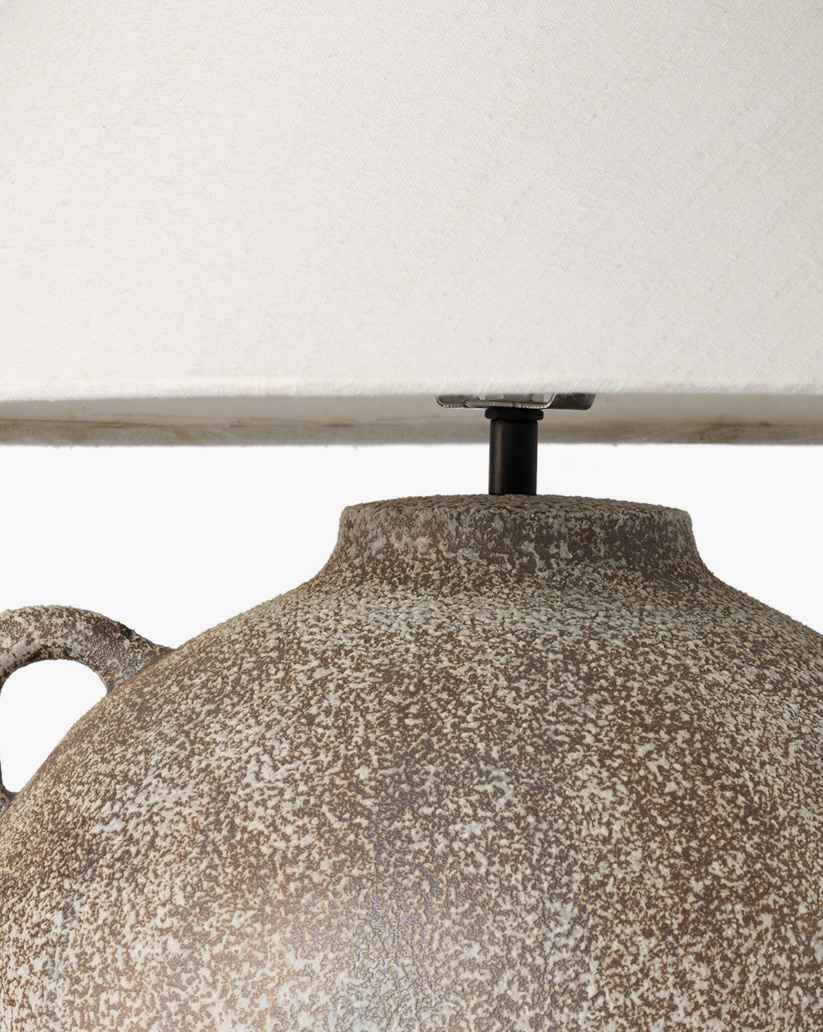 Close-up of the Mays Table Lamps textured, speckled ceramic base—evoking vintage clay jars—paired with a light beige fabric shade. The image focuses on the upper base and lower edge of the lampshade, by McGee & Co.