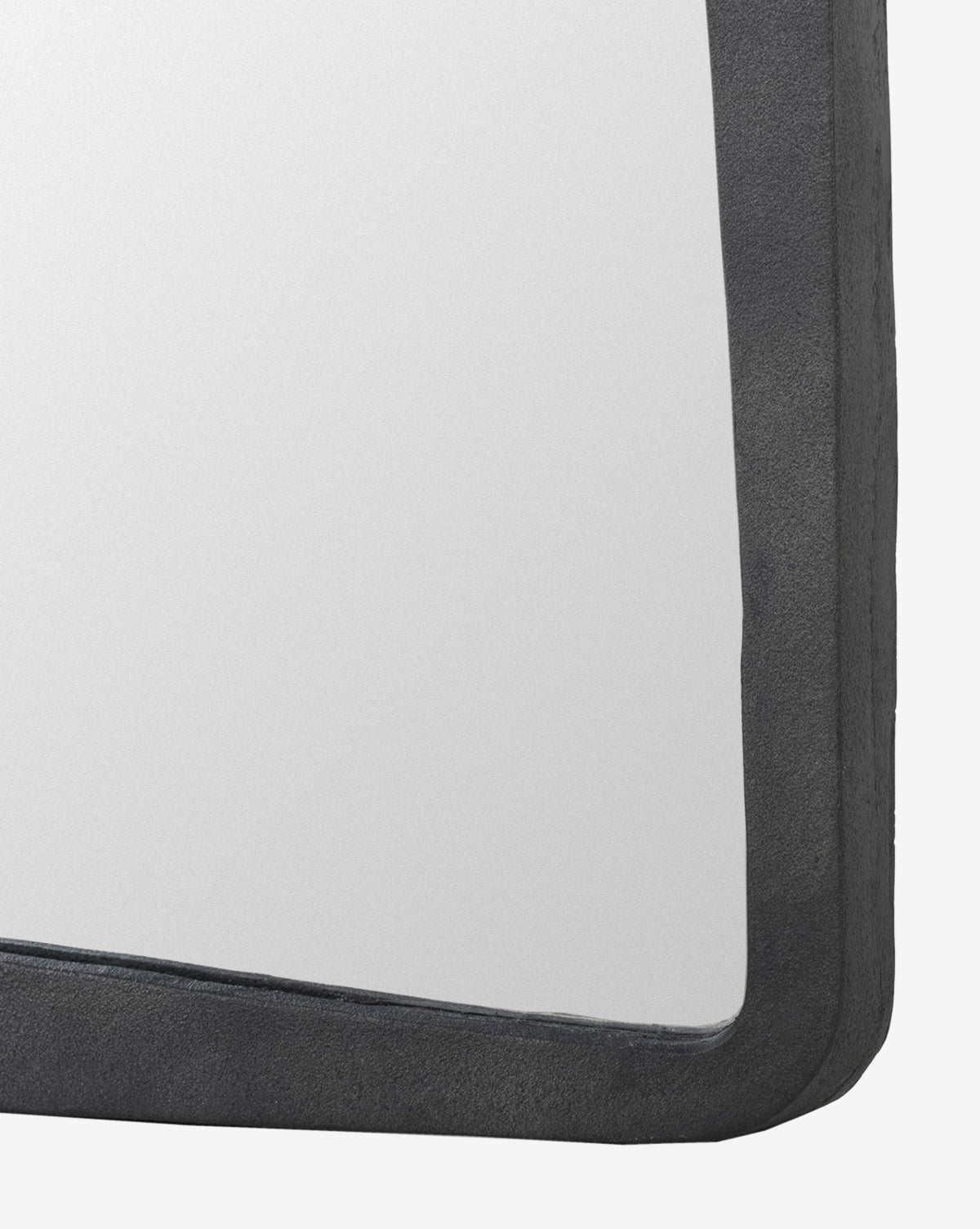 Close-up of the top right corner of the Penrod Floor Mirror, featuring a thick, dark, textured cast aluminum frame. The mirror reflects a plain, light background—blending function and sculptural style in home decor, by McGee & Co.