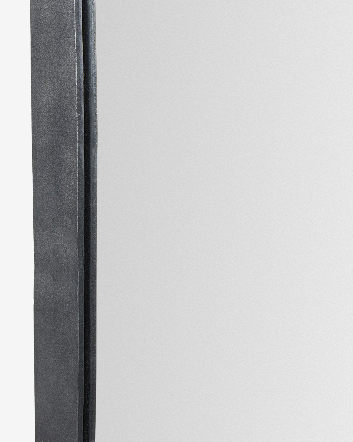 A close-up of the Penrod Floor Mirror shows its dark, textured cast aluminum frame along the left edge, while the right side reflects a blank, light surface, by McGee & Co.