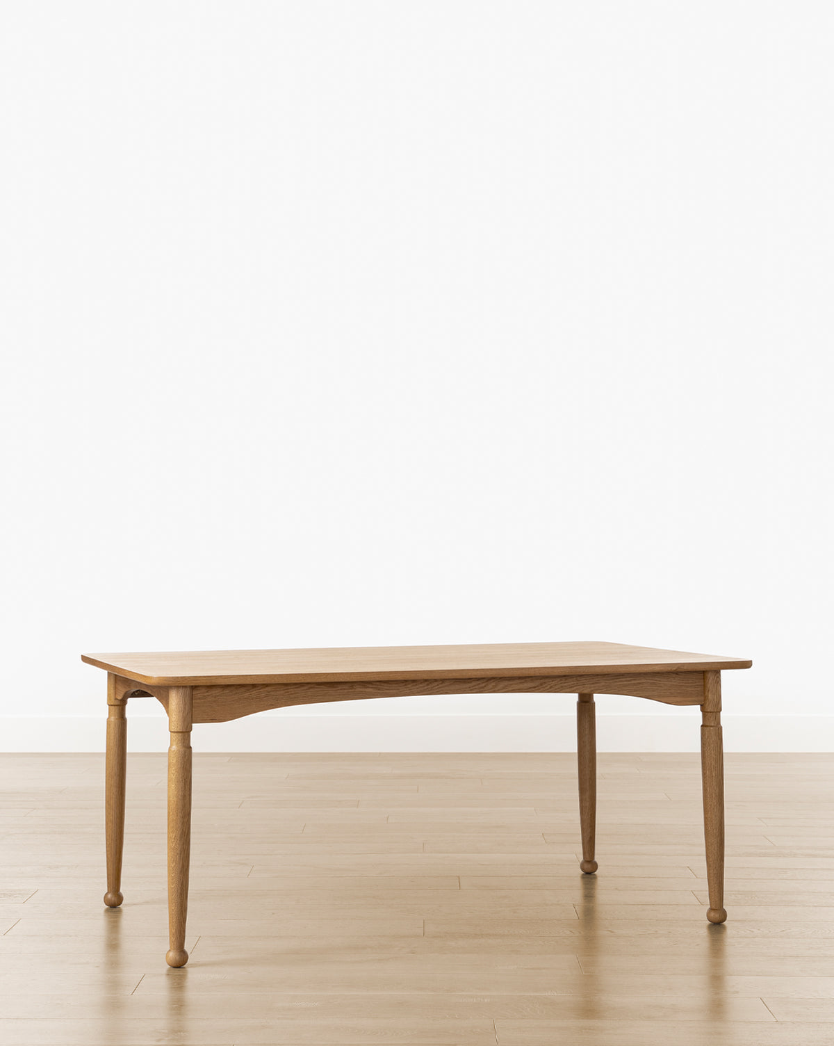 The Phipps Dining Table features four turned legs and stands on a light wood floor against a plain white background, blending modern traditional design with timeless appeal, by McGee & Co.
