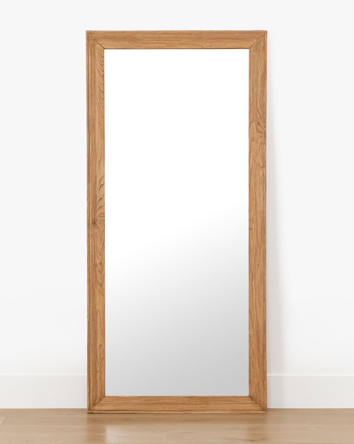 The Pippen Floor Mirror showcases a large rectangular shape and a natural wood frame in honey elm finish, perfect for leaning upright against any wall, by McGee & Co.