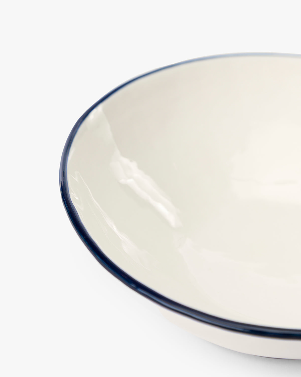 Close-up of a white enamel Pritchard Bowls (Set of 4) with a navy rim and creamy glaze, shown against a plain white background. Only part of the bowl’s edge is visible, by McGee & Co.