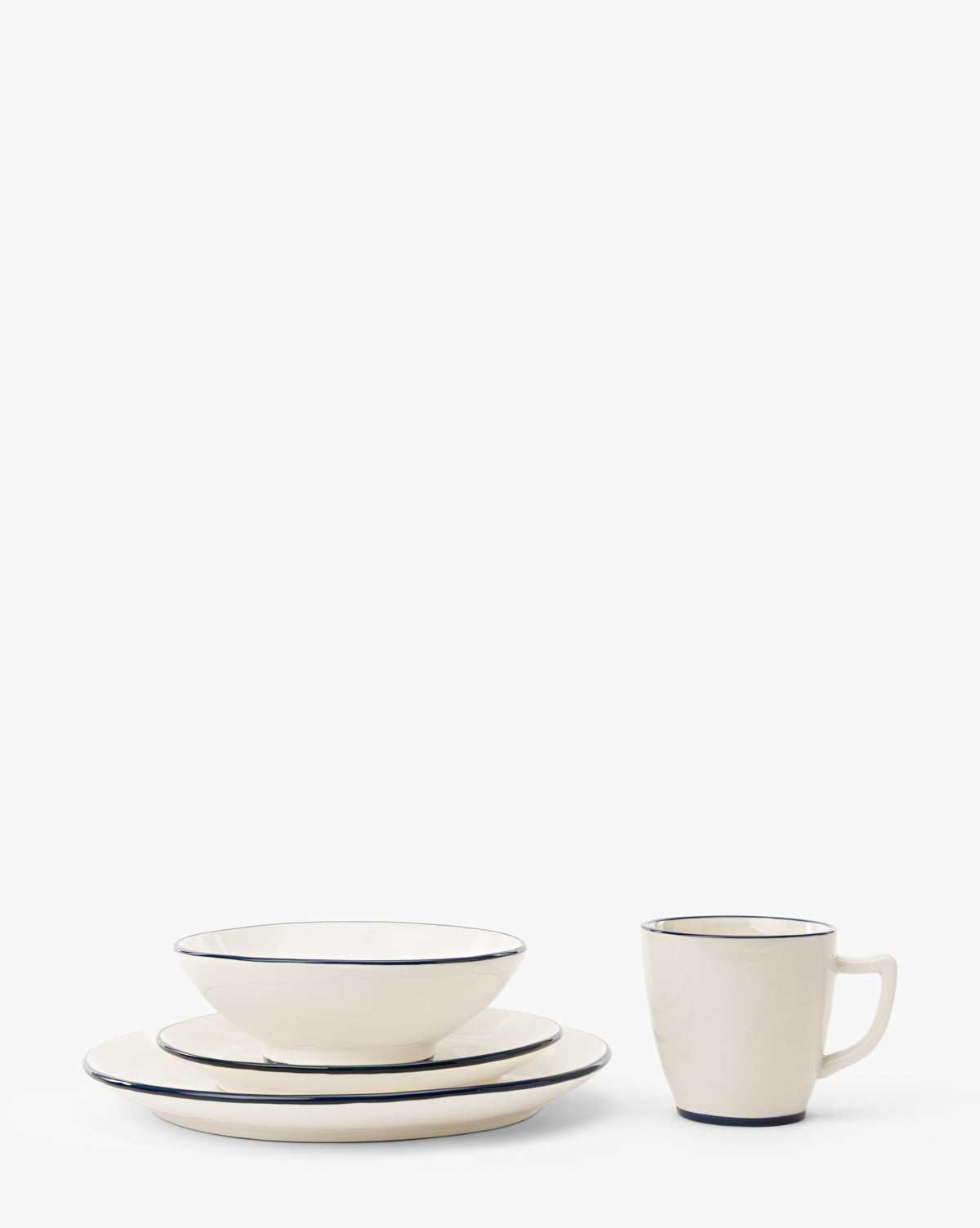 The Pritchard Serving Bowl, paired with two cream plates of different sizes and a mug—all featuring a thin dark rim—is arranged neatly on a white background, by McGee & Co.