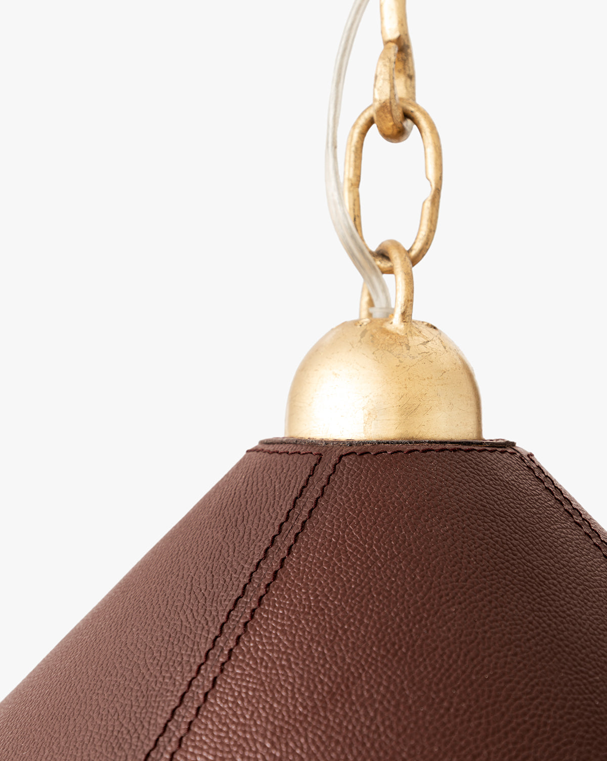 Close-up of the Scarlett Pendant, an elegant light with brown textured leather and visible stitching, topped by a gold leafed iron cap and chain, shown against a plain white background, by McGee & Co.