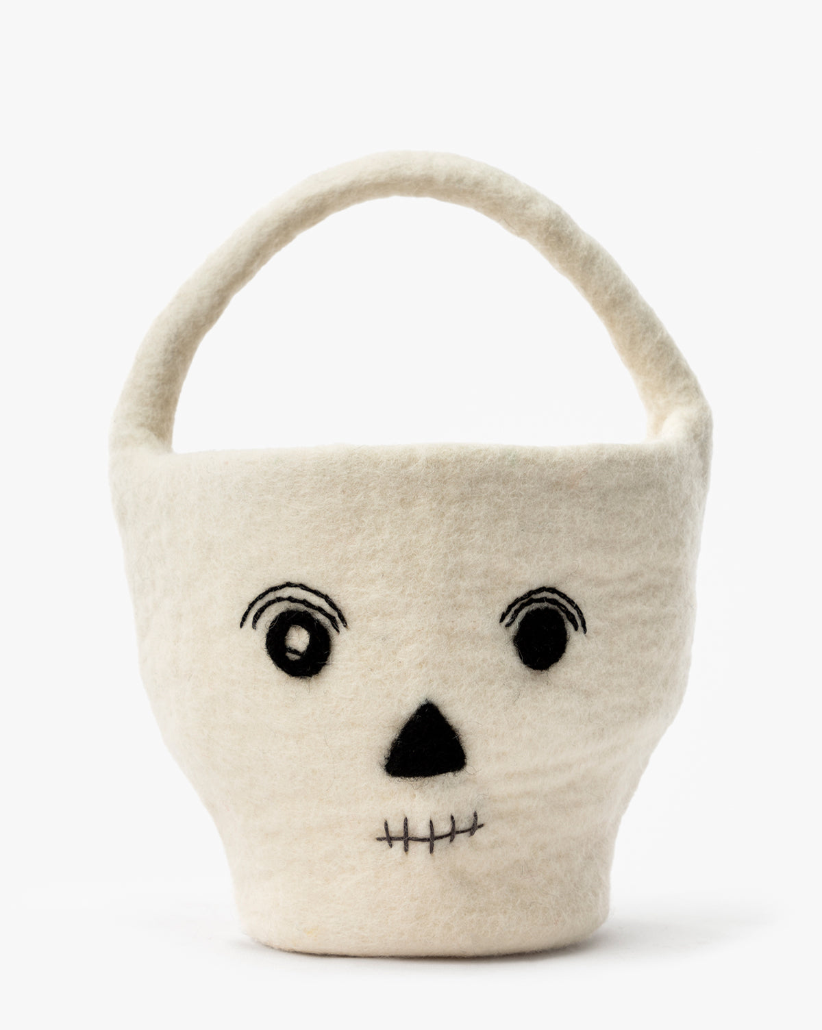 The Skeleton Trick or Treat Felt Basket is a cream felt basket with a handle, decorated with a stitched black skull face—ideal for Halloween or use as a festive Skeleton Trick or Treat Basket, by McGee & Co.