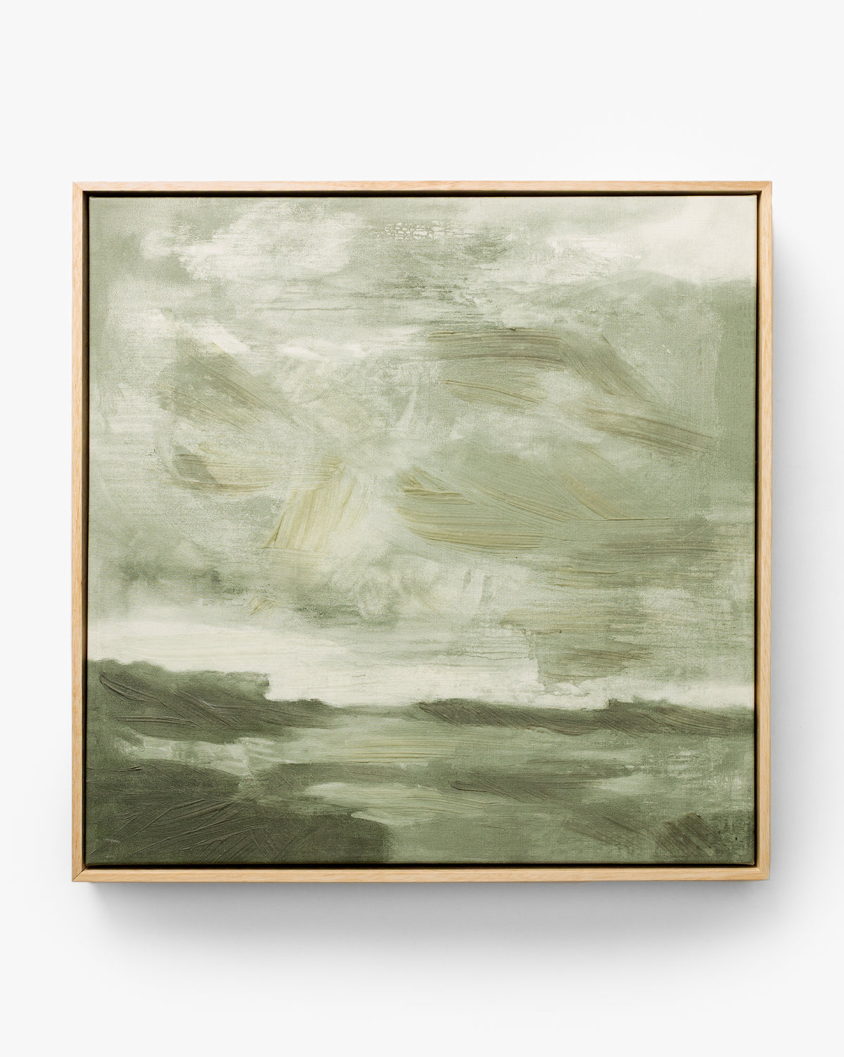 Stormy Sky Afternoon is an abstract painting in green and white with soft, blurred brushstrokes recalling a cloudy sky over a landscape. This framed wall art features light-colored wood for a modern accent, by McGee & Co.
