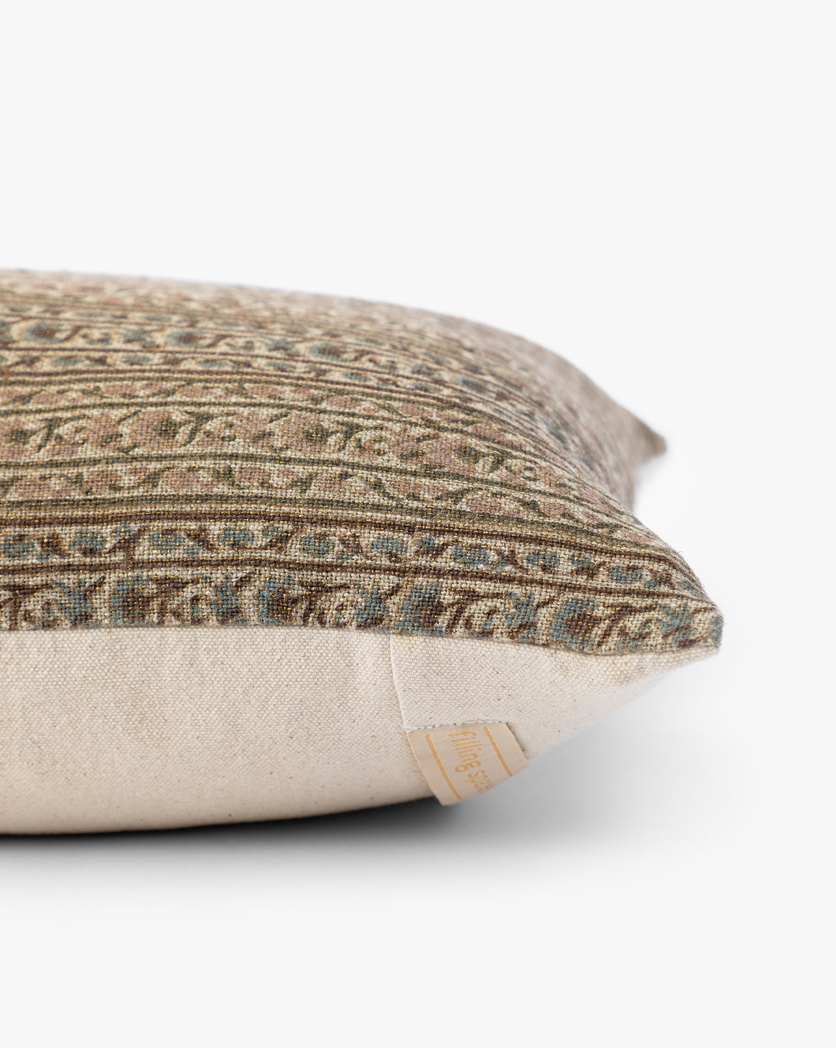 A close-up side view of the Wakefield Pillow Cover showcases its textured, patterned fabric in earthy tones, beige underside, and a small fabric tag on the seam, by McGee & Co.