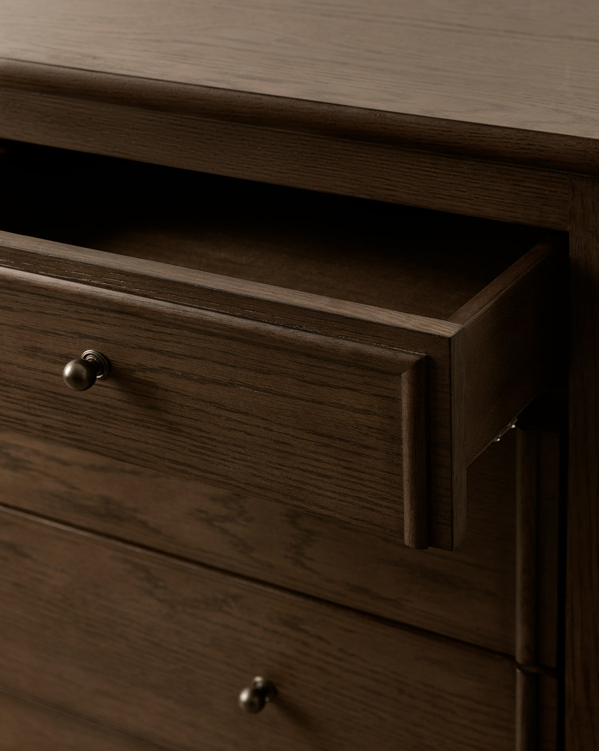 A close-up of the Yorkshire Dresser showcases its English oak finish and metal knobs. The partially open top drawer reveals spacious bedroom storage inside, by McGee & Co.